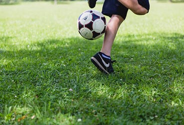 A child performing skills using a Football on a green field